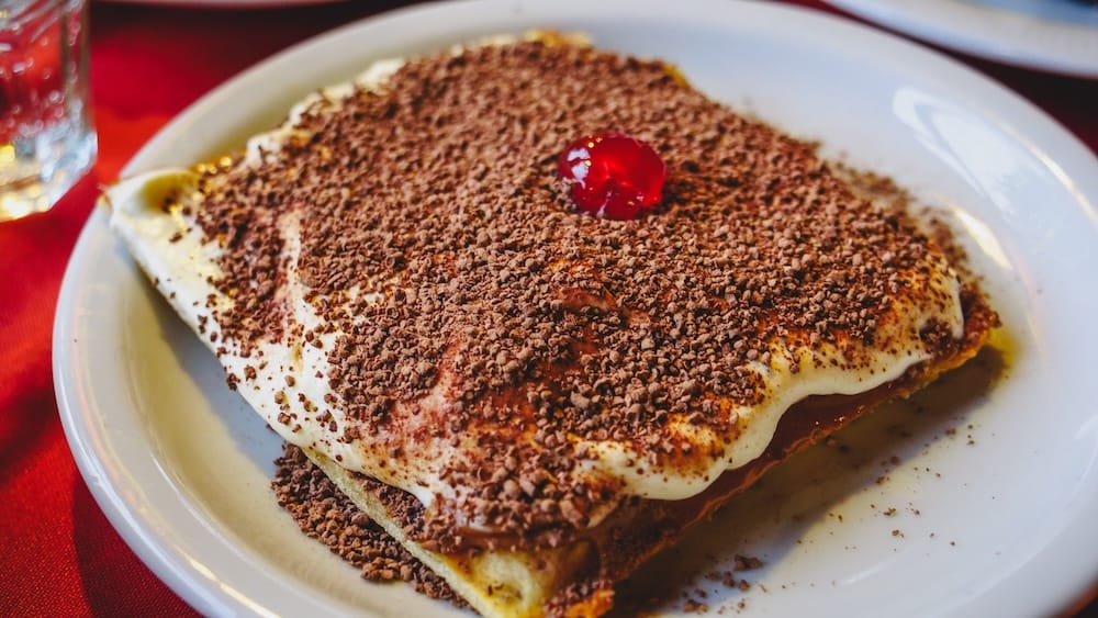Dulce de leche waffles in Esquel topped with whipped cream, grated chocolate, and a cherry, a rich Patagonian dessert enjoyed as a calorie-heavy reward after exploring town or braving the region’s wind and cold
