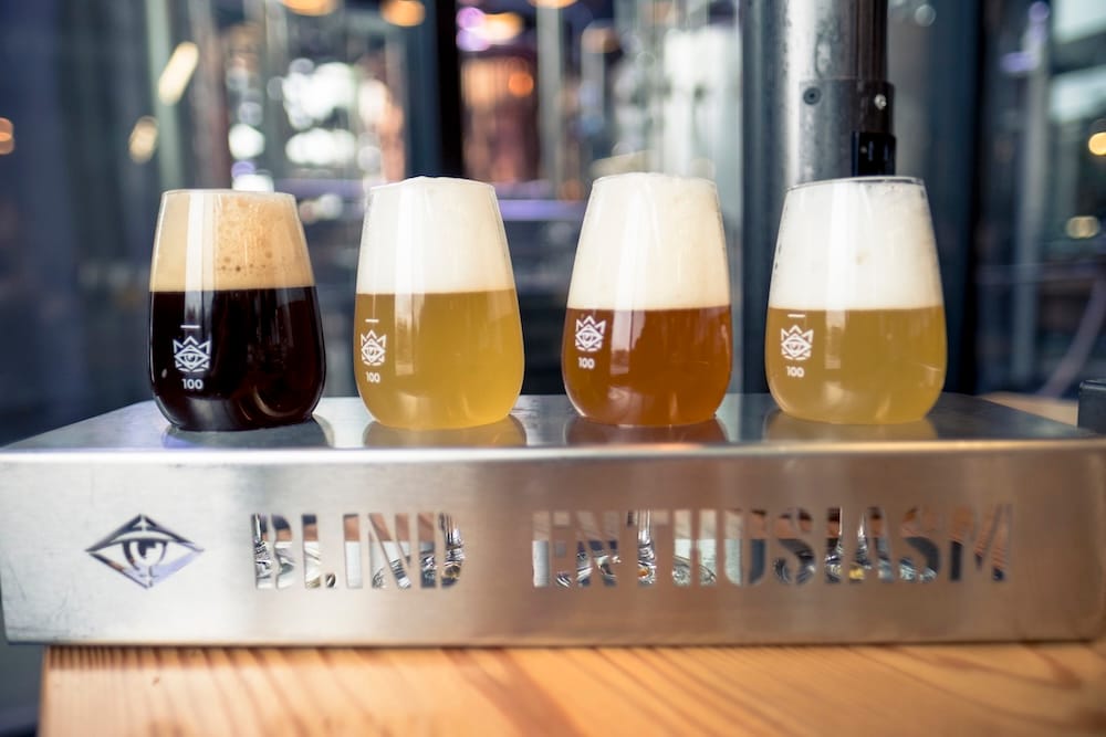 Una degustación de cuatro cervezas artesanales en Edmonton, Alberta, Canadá, desde marrón oscuro hasta dorado pálido y ámbar, servidas en vasos de cata con marca sobre una bandeja metálica en una cervecería.