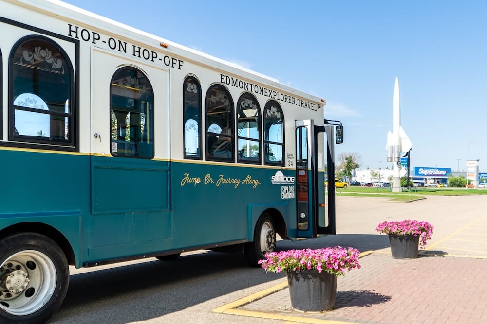 Edmonton Explorer hop-on hop-off sightseeing trolley in Edmonton, Alberta, Canada Edmonton Explorer hop-on hop-off sightseeing trolley parked in Edmonton, Alberta, Canada, with its green-and-cream body, open passenger door, flower planters and a clear blue summer sky.