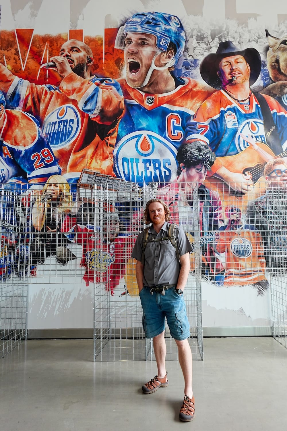 Samuel Jeffery está frente a un gran mural de los Edmonton Oilers en Edmonton, Alberta, Canadá, rodeado de imágenes de hockey y colores del equipo dentro del distrito de eventos de la ciudad.