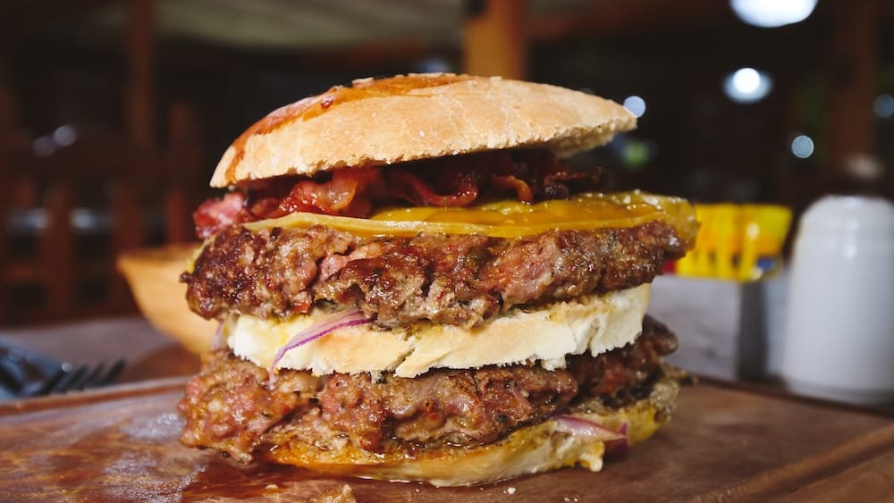 Double-patty gourmet burger with melted cheese and bacon in El Calafate, Patagonia, Argentina, representing the high-calorie food culture that pairs perfectly with local craft beer after long days of glacier excursions and Patagonian winds.
