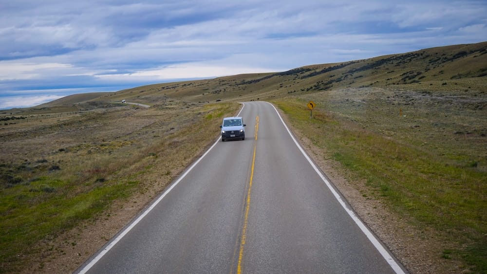 Bus traveling along a remote Patagonian highway toward El Calafate, crossing exposed steppe terrain where strong crosswinds can affect driving stability and long-distance transport, highlighting how Patagonia’s weather directly impacts road travel and logistics.

