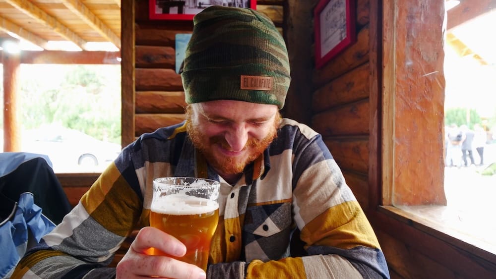 Samuel Jeffery drinking a pint of Patagonian craft beer inside a rustic wooden bar in El Calafate, Argentina, capturing the relaxed post-adventure reward culture that makes beer such a natural part of travel life across Patagonia.
