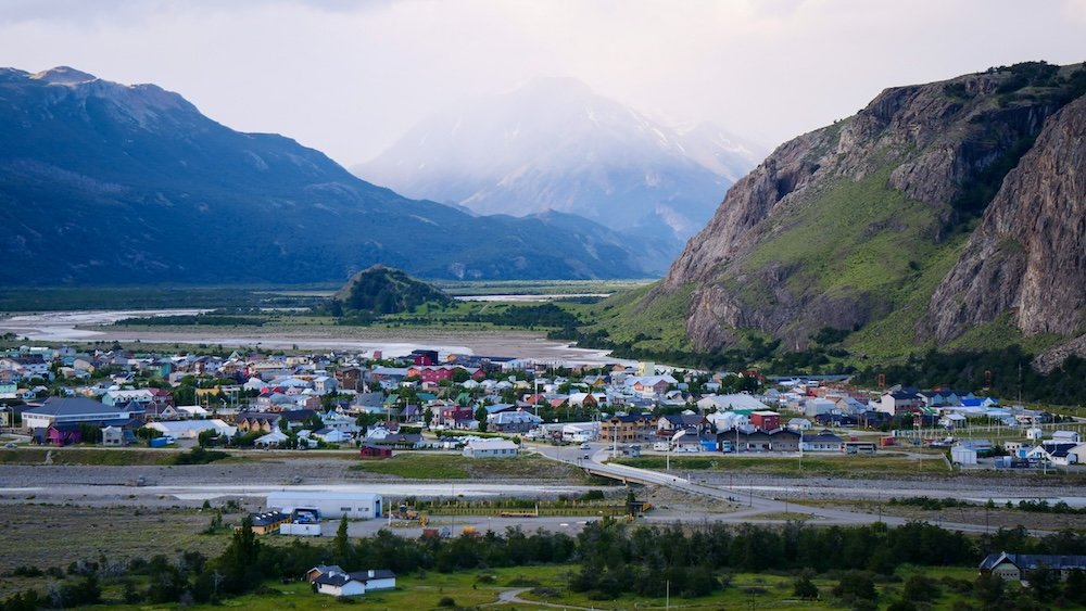 El Chaltén, Argentina with colorful houses clustered beneath towering Patagonian mountains and cliffs, highlighting the town’s remote frontier atmosphere where dramatic nature completely dominates the landscape and human settlement feels small by comparison.