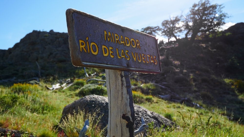 El Chaltén, Argentina trail sign for Mirador Río de las Vueltas beside rocky terrain and Patagonian scrub, marking a short, easy hike that rewards visitors with valley views and a quick scenic win near town.
