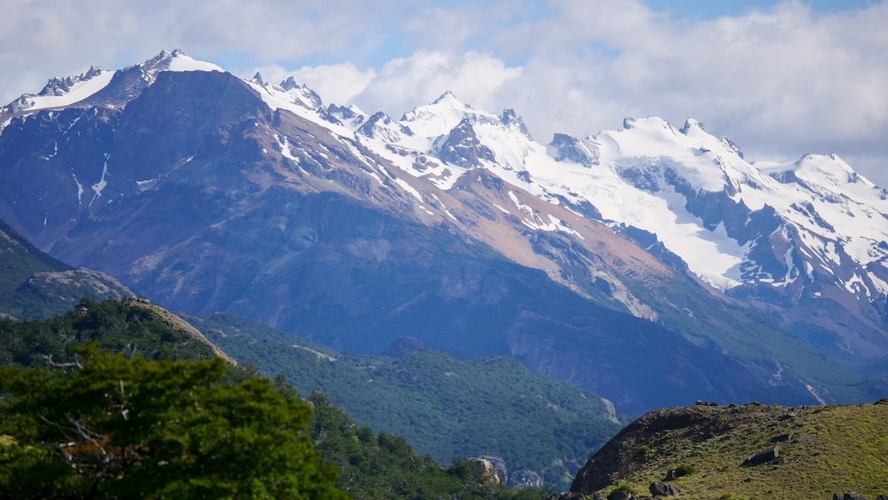 El Chaltén, Argentina with sweeping Patagonian mountain scenery, jagged snow-capped peaks, layered green valleys, and rugged hills seen from an easy hiking trail, showing why even short walks deliver dramatic views in Los Glaciares National Park.

