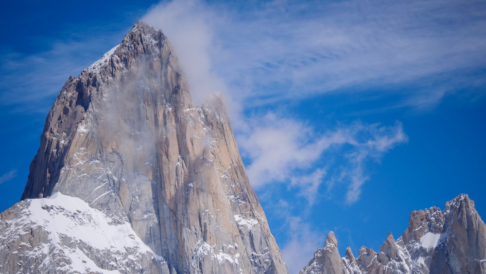 El Chaltén Fitz Roy mountain peak in Patagonia, Argentina, featuring dramatic granite spires dusted with snow rising above forested valleys under a bright blue sky, showcasing one of South America’s most iconic hiking landscapes.