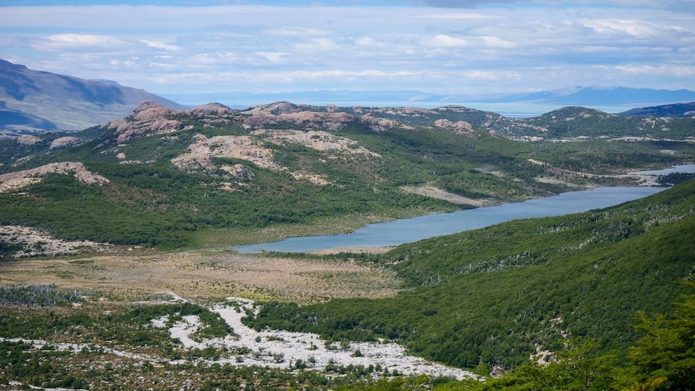 Diverse landscape on an El Chaltén hike, with a winding river cutting through green valleys, rocky hills, and open steppe terrain—showcasing the variety of scenery hikers experience beyond the famous Fitz Roy viewpoints.
