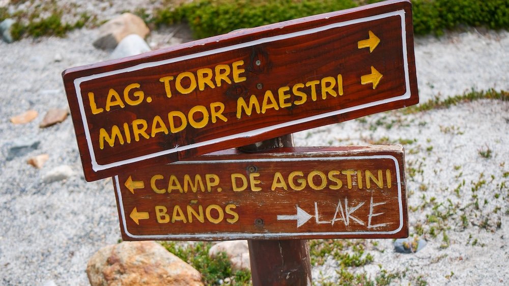 El Chaltén, Argentina trail sign pointing toward Laguna Torre and Mirador Maestri, with wooden arrows indicating directions to Campamento De Agostini and baños, highlighting the well-marked hiking routes inside Los Glaciares National Park.
