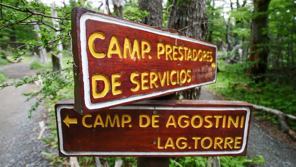 El Chaltén, Patagonia, Argentina trailhead sign pointing toward Camp de Agostini and Laguna Torre, marking the forest path used by hikers and campers linking iconic multi-day trekking routes in the national park