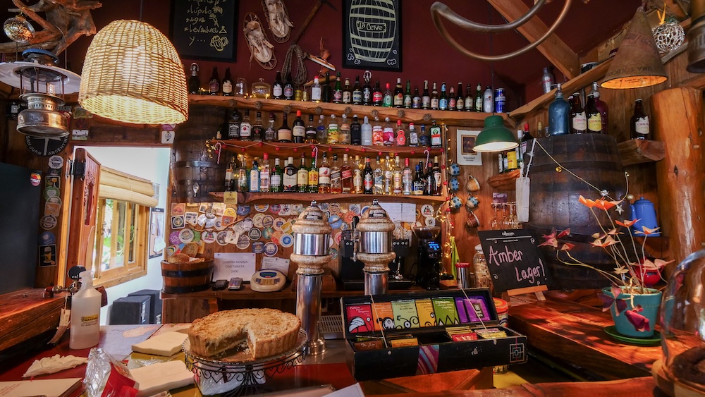 El Chaltén, Patagonia, Argentina: a warm and cozy café interior with wooden bar, hanging lamps, craft beer taps, and homemade cake on the counter, the perfect place to relax on a slow rest day.
