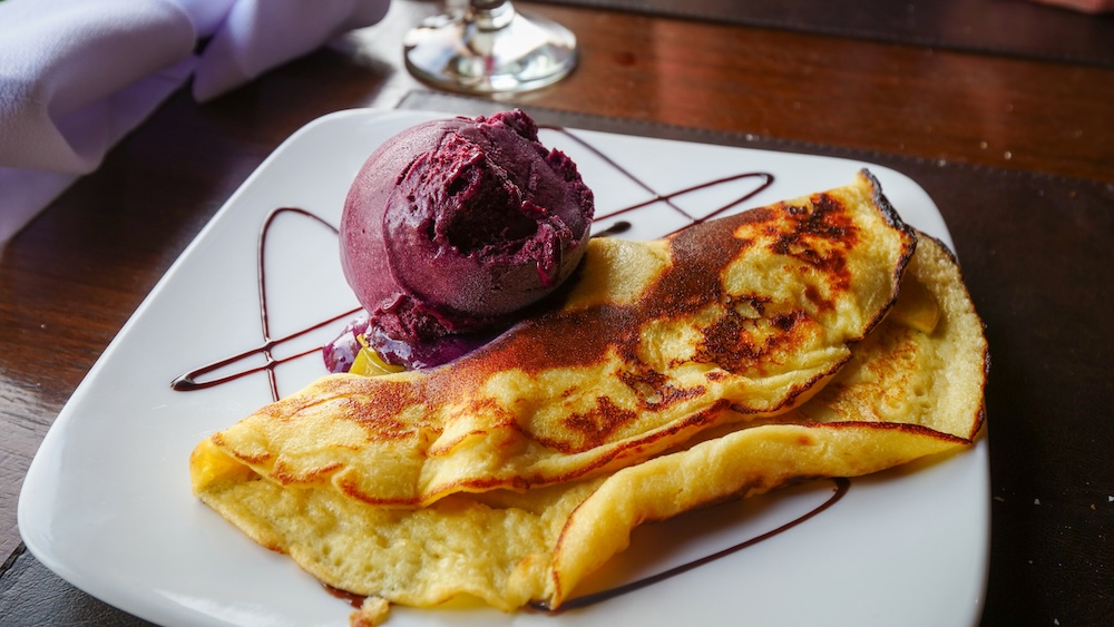 Crepe and berry ice cream dessert trail stop in El Chaltén El Chaltén, Patagonia, Argentina — a golden crepe paired with berry ice cream and chocolate drizzle, part of hitting the dessert trail hard after a long day hiking Patagonia’s rugged mountain paths.