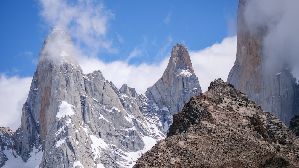 Mount Fitz Roy in El Chaltén, Patagonia, Argentina, with jagged granite spires dusted with snow as moody clouds swirl around the peaks under shifting blue skies, creating a dramatic Patagonian atmosphere
