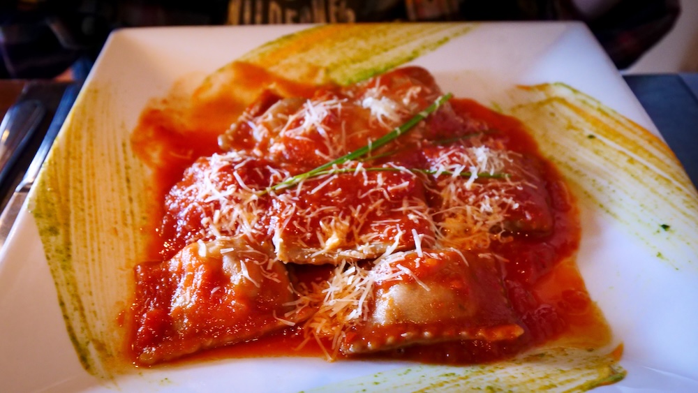 El Chaltén, Patagonia, Argentina: a gourmet ravioli dish in rich tomato sauce topped with parmesan on a white plate, a comforting rest-day dinner to refuel after big hikes in Patagonian weather.