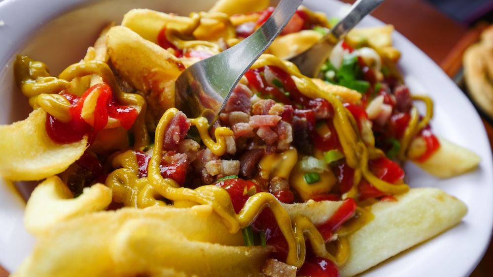 Greasy post-hike comfort food in El Chaltén El Chaltén, Patagonia, Argentina — a close-up of crispy fries loaded with bacon, melted cheese, and sauces, a greasy and satisfying comfort meal perfect for hikers craving a hearty post-trail reward in town.