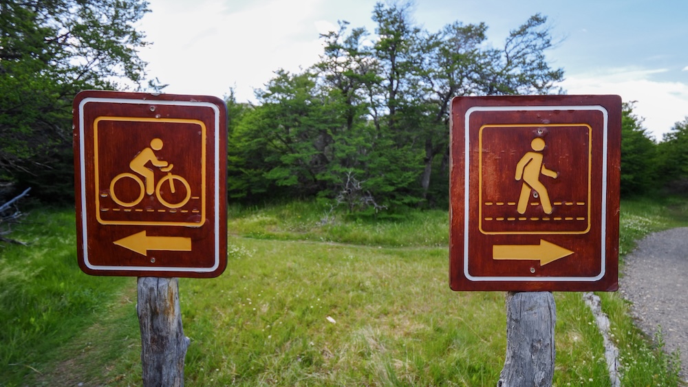 Hiking or biking trail sign dilemma in El Chaltén, Patagonia, Argentina El Chaltén, Patagonia, Argentina: two wooden trail signs point in opposite directions—one for biking and one for hiking—capturing the classic outdoor dilemma facing visitors choosing how to explore the national park.