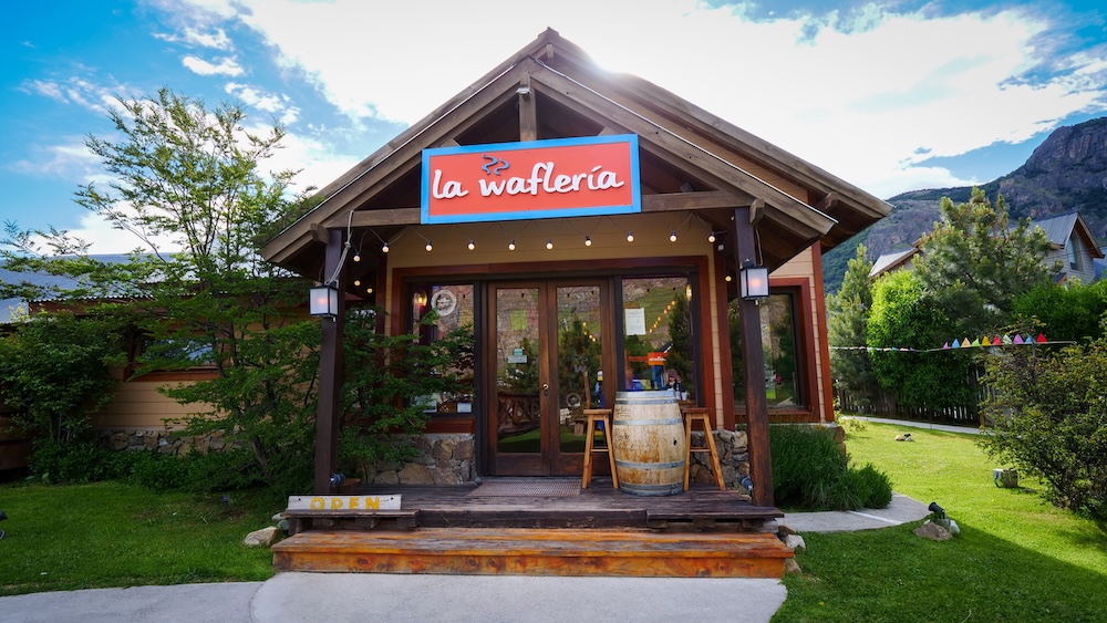 La Waflería waffle institution in El Chaltén El Chaltén, Patagonia, Argentina — the wooden storefront of La Waflería with its bright sign and garden seating, a true local institution serving famous waffles to hikers after long days on the trails.