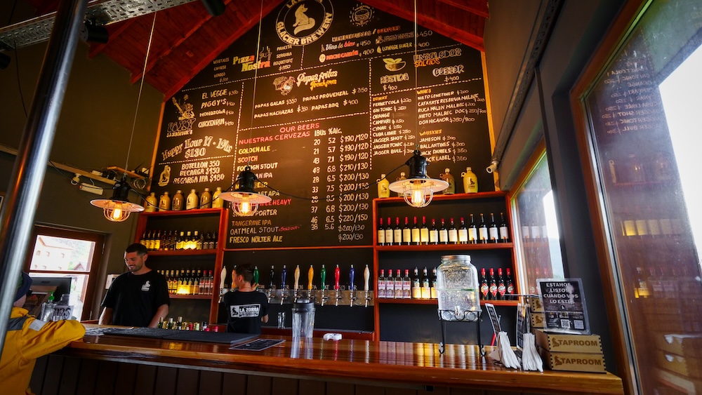 Friendly bar scene at La Zorra Taproom in El Chaltén El Chaltén, Patagonia, Argentina — the friendly bar scene inside La Zorra Taproom with chalkboard beer menu, craft taps, and hikers gathering for post-trail drinks in a lively mountain pub atmosphere.