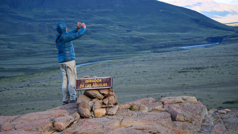El Chaltén, Patagonia, Argentina viewpoint at Mirador de las Águilas, showing a traveler photographing the vast valley below, illustrating a short but exposed hiking climb with a rewarding scenic payoff
