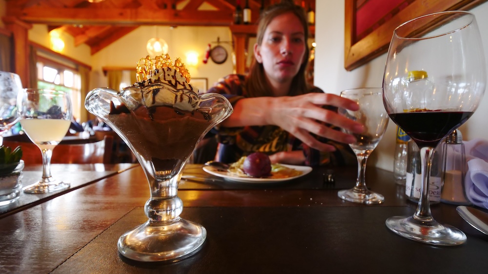 Chocolate mousse and wine at Senderos in El Chaltén with Audrey Bergner El Chaltén, Patagonia, Argentina — Audrey Bergner reaches for a glass of wine beside an elegant chocolate mousse at Senderos, savoring a well-earned post-hike dessert after a long day on Patagonia’s mountain trails.
