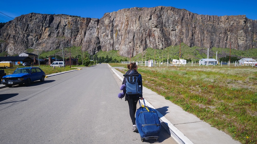 El Chaltén, Patagonia — Audrey Bergner rolling luggage along the road from the bus station toward Vertical Lodge, capturing a realistic budget travel moment arriving in Argentina’s hiking capital.