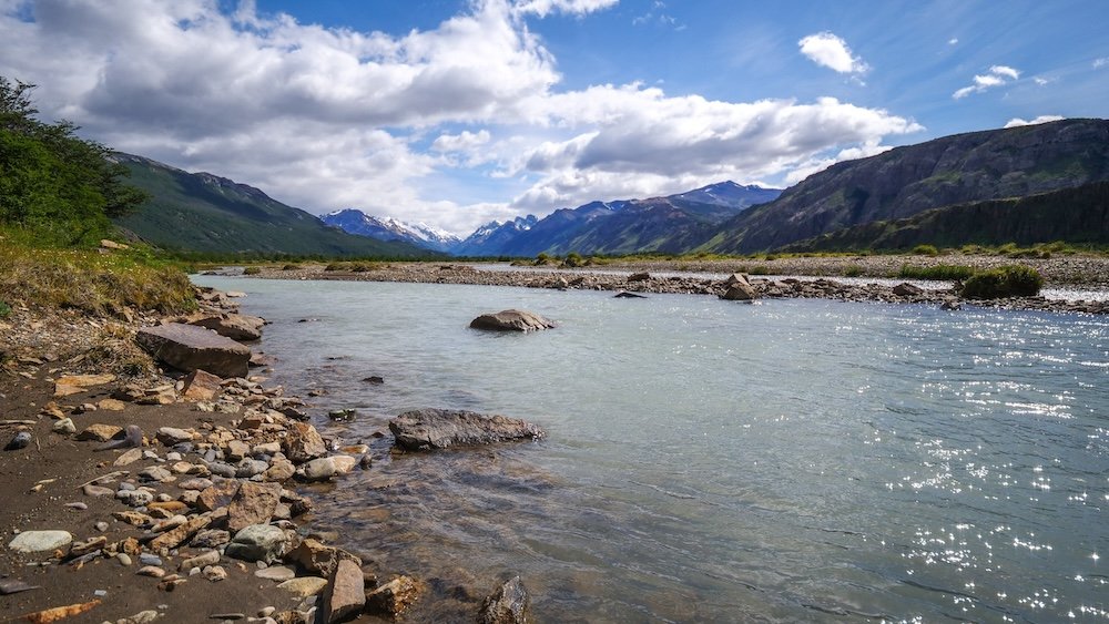 Chorrillo del Salto area in El Chaltén, Patagonia, with a calm glacial river flowing through a wide valley framed by green hills and distant Andean peaks, offering relaxed scenery on one of the region’s easiest walks.
