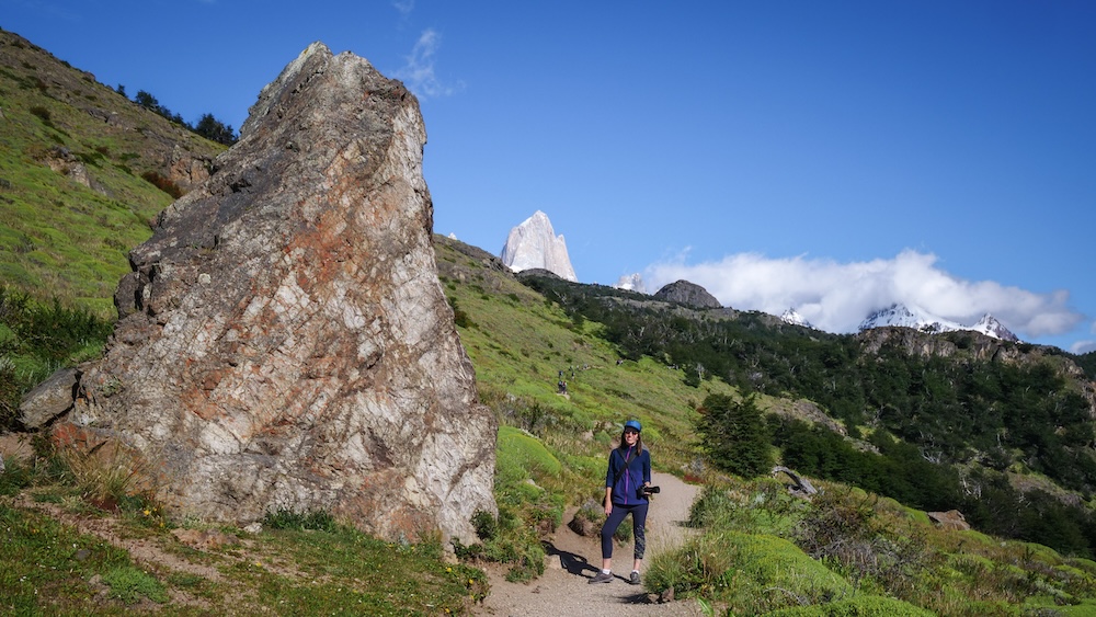 El Chaltén Patagonia Laguna de los Tres hiking with Audrey Bergner El Chaltén, Patagonia trail at Laguna de los Tres with Audrey Bergner hiking, towering Fitz Roy peak in the background, showcasing a scenic mountain path, rocky outcrop, and clear-weather trekking experience in Patagonia.
