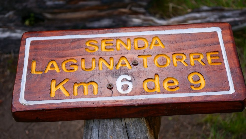 Laguna Torre trail sign in El Chaltén reading “Senda Laguna Torre Km 6 de 9,” marking steady progress along the hike toward Cerro Torre and highlighting the well-marked distance signage that helps hikers pace themselves on this classic Patagonian trek.