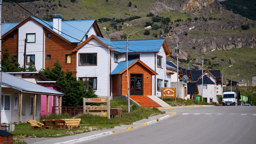 Street view of El Chaltén Patagonia trekking town in Los Glaciares National Park El Chaltén Patagonia small mountain town street with colorful lodges, hostels and houses beneath rugged hills in Los Glaciares National Park, illustrating the quiet trekking basecamp atmosphere of Argentina’s famous hiking village.