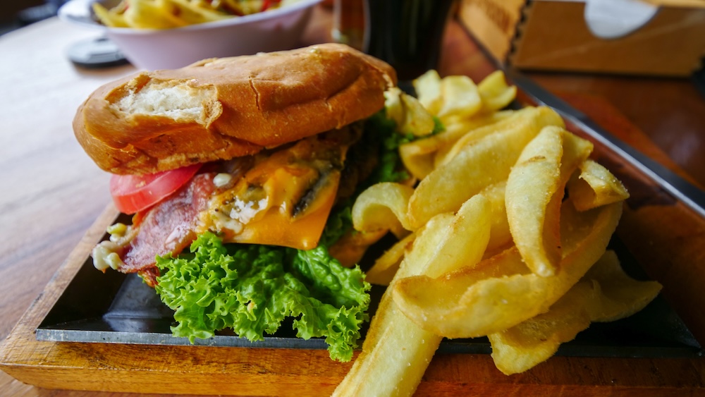 El Chaltén Patagonia post-hike meal at La Zorra Taproom featuring a greasy burger with bacon, cheese and fries, the kind of high-calorie comfort food exhausted hikers crave after long treks like the Fitz Roy or Laguna Torre hikes.