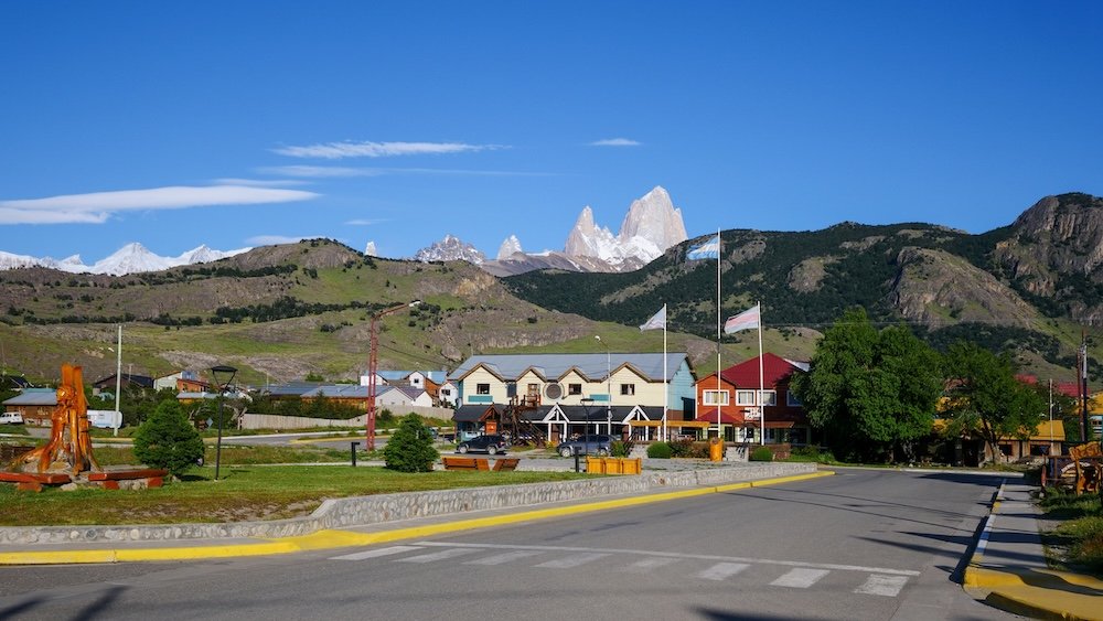 El Chaltén in summer with postcard-perfect weather, showing colorful buildings, quiet streets, and Mount Fitz Roy rising sharply in the background under clear blue skies—capturing the charm and dramatic scenery that define Argentina’s trekking capital.