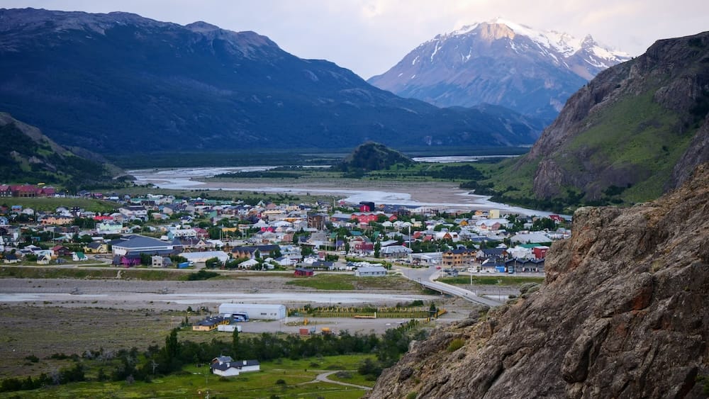 El Chaltén Patagonia town viewed from a high hillside vantage point with the Río de las Vueltas valley and snowcapped Andes mountains surrounding the trekking capital of Argentina near Los Glaciares National Park.