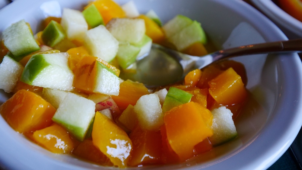 A fresh fruit salad breakfast at Vertical Lodge in El Chaltén, Patagonia, Argentina, featuring chopped mango, apple, and melon in a white bowl, part of a healthy early-morning meal before a long hiking day.