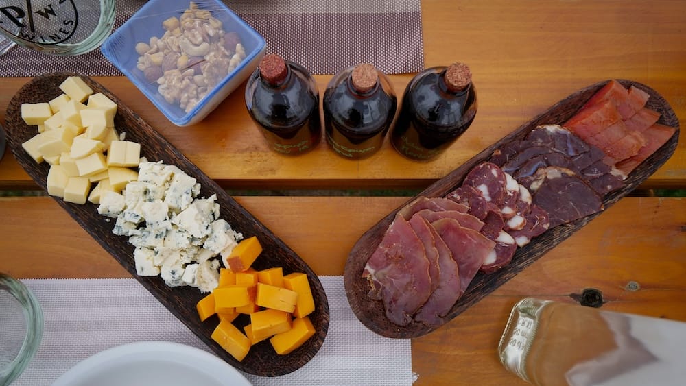 Vineyard picnic with Patagonian cheeses, charcuterie and red wine tasting vials in El Hoyo, Chubut, Argentina Overhead view of a vineyard picnic in El Hoyo, Chubut, Patagonia, Argentina, with local cheeses, cured meats, mixed nuts and three corked red wine tasting vials arranged on a wooden table.