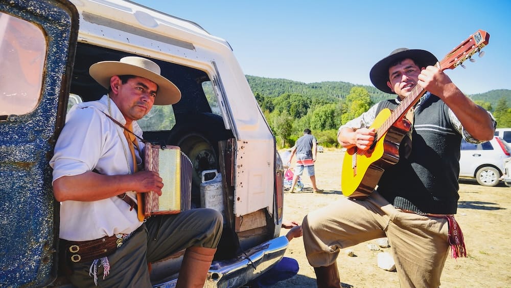 Gaucho musicians El Manso Patagonia folk music rural festival El Manso near El Bolsón Patagonia gaucho musicians playing guitar and accordion beside a dusty vehicle, capturing informal folk music gathering at a rural festival where culture happens organically rather than as a staged performance.