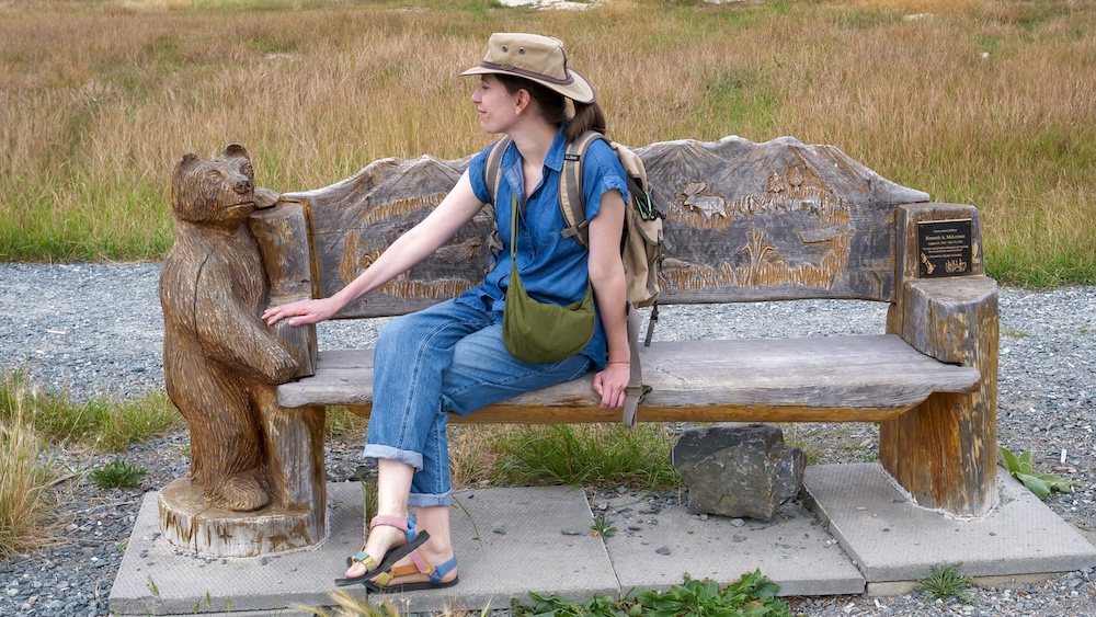 Elizabeth Lake in Cranbrook, BC featuring a family-friendly park bench with a carved wooden bear, showing That Backpacker Audrey Bergner taking a relaxed break along the trail, highlighting playful details, rest stops, and the welcoming atmosphere that makes this lake easy to enjoy with kids.
