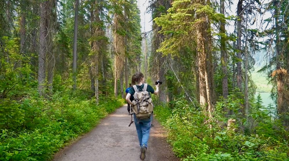 Audrey Bergner walking the Emerald Lake lakeshore trail in Yoho National Park, British Columbia, Canada Audrey Bergner walks the Emerald Lake lakeshore trail in Yoho National Park, British Columbia, Canada, carrying a backpack through dense evergreen forest with glimpses of green lake water beside the path.