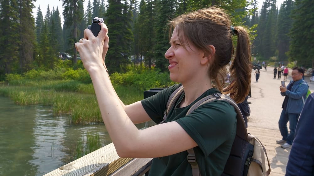Audrey Bergner photographing Emerald Lake in Yoho National Park, British Columbia, Canada Audrey Bergner photographs the shoreline at Emerald Lake in Yoho National Park, British Columbia, Canada, standing beside calm water and reeds with evergreen forest surrounding the lakeside path.