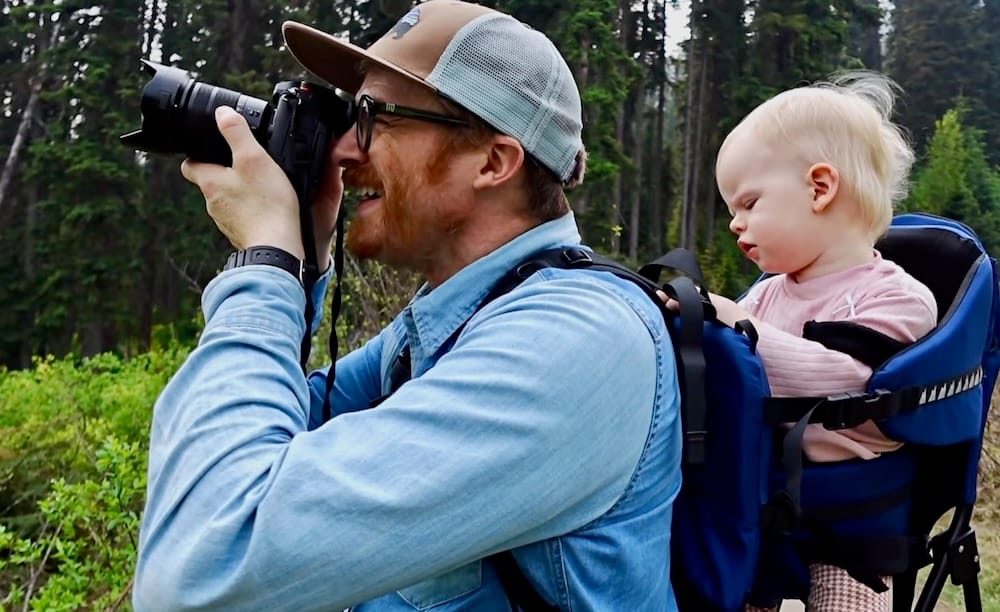 Samuel Jeffery photographing Emerald Lake in Yoho National Park with Aurelia Jeffery in a child carrier Samuel Jeffery photographs Emerald Lake in Yoho National Park, British Columbia, Canada, while carrying Aurelia Jeffery in a child backpack beside dense Canadian Rockies forest.