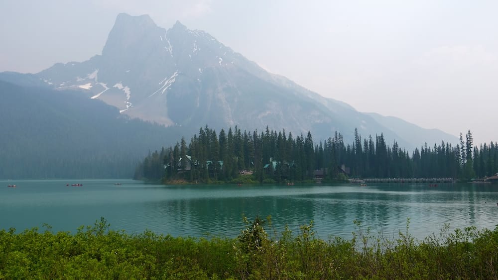 Scenic Emerald Lake view in Yoho National Park, British Columbia, Canada, with canoes and lakeside buildings Scenic view across Emerald Lake in Yoho National Park, British Columbia, Canada, with green water, small red canoes, forested shoreline buildings and steep Canadian Rockies mountains rising behind them.