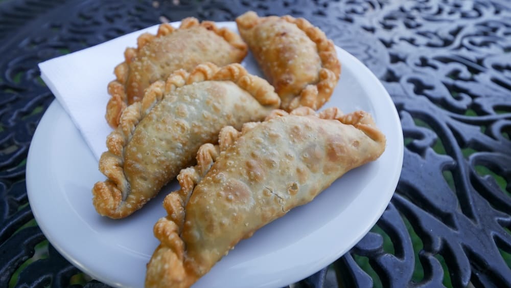 Empanadas doradas fritas en un plato blanco en la Patagonia, Argentina, mostrando los bordes de masa crujiente con burbujitas, el clásico repulgue sellado. Un clásico salado para llevar que suele acompañar el mate.