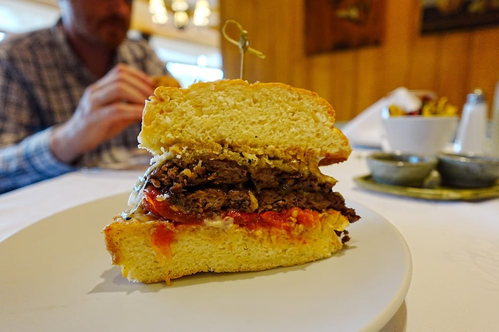 Double Angus Burger at Espacio Lago Moreno, Llao Llao Hotel, Bariloche, Río Negro, Patagonia, Argentina Close-up of a double Angus burger served at Espacio Lago Moreno inside Llao Llao Hotel in Bariloche, Río Negro, Patagonia, Argentina, with two beef patties, tomato, melted cheese and thick bread on a white plate.