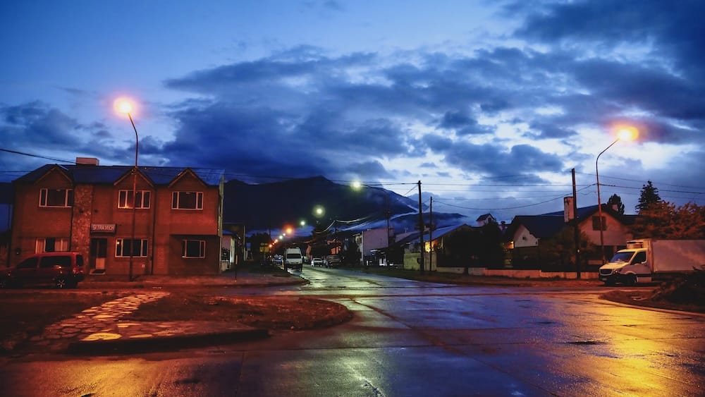 Early Morning Outside Esquel Bus Station in Chubut, Patagonia, Argentina After an Overnight Bus Wet streets glow under orange lamps outside the Esquel bus station in Chubut, Patagonia, Argentina, during the dim early morning after an overnight journey beneath heavy clouds and distant hills.