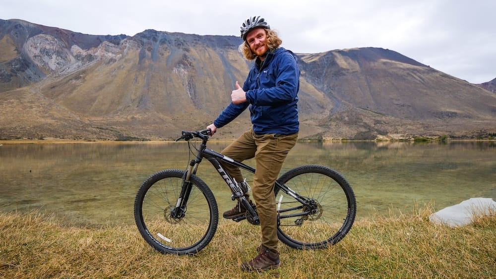 Esquel Patagonia mountain biking with Samuel Jeffery scenic lake Andes cycling adventure Esquel, Patagonia Argentina — Samuel Jeffery riding a mountain bike beside a calm lake with rugged Andean hills in the background, highlighting outdoor adventure, cycling routes, and the scenic natural landscapes that define this Patagonian destination.