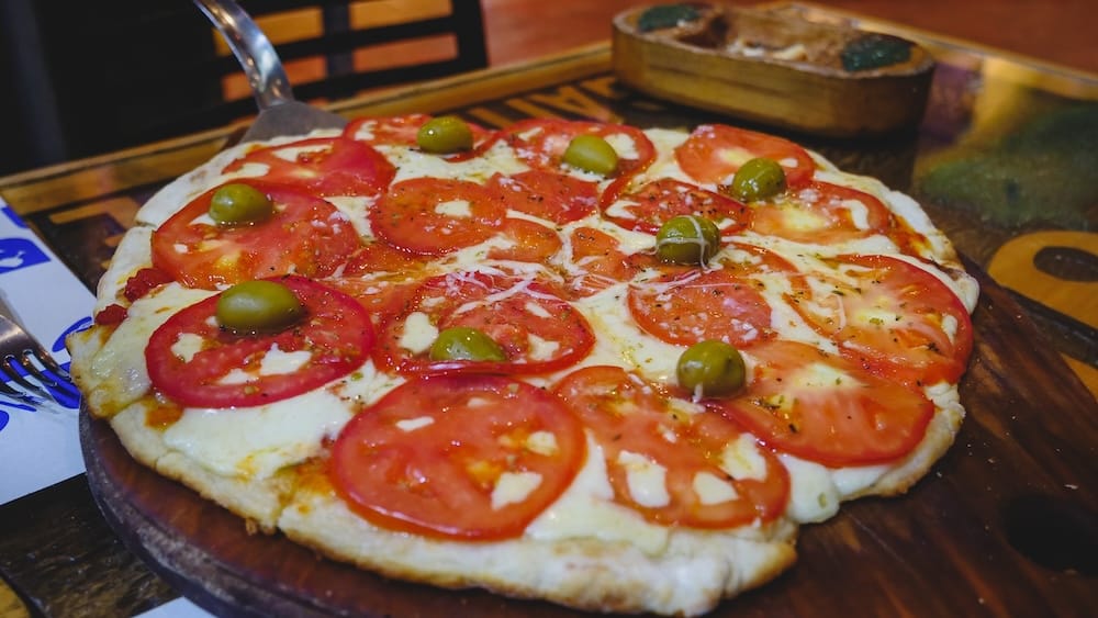 Esquel Patagonia Argentina Patagonian pizza with thin crust fresh tomato slices olives and melted cheese on a wooden board highlighting balanced toppings and rustic a la piedra style distinct from thick Buenos Aires pizza