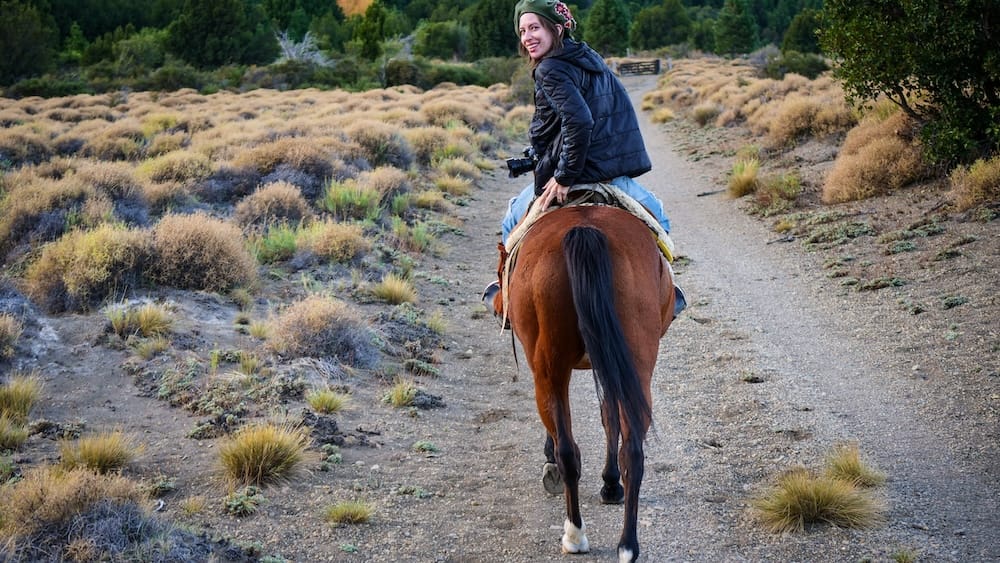 Audrey Bergner mira hacia atrás por encima del hombro mientras cabalga por un sendero de estepa bordeado de matorrales en Estancia Arroyo Verde, cerca de Villa Traful, Neuquén, en la Patagonia argentina.