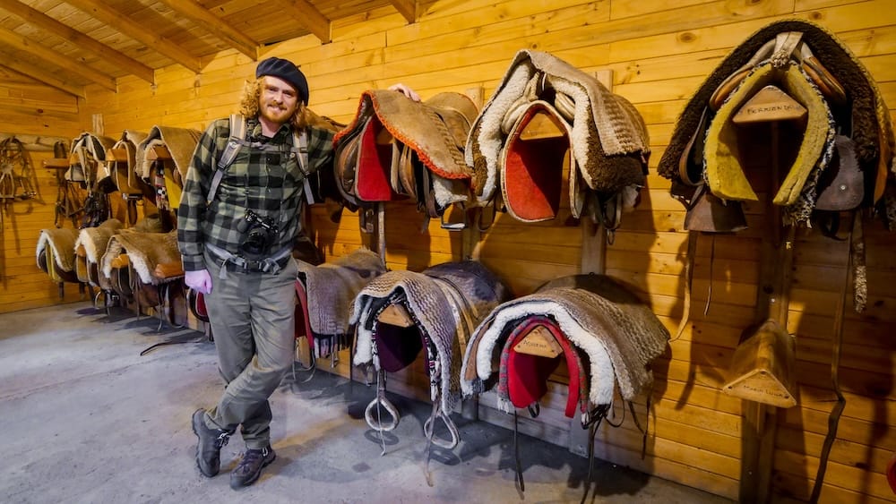 Samuel Jeffery está parado en una sala de monturas de madera, con filas de monturas de cuero tradicionales, en Estancia Arroyo Verde, cerca de Villa Traful, Neuquén, en la Patagonia argentina.