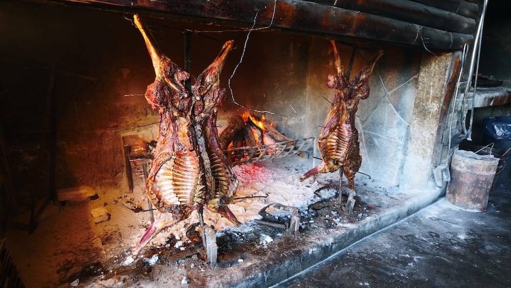 Patagonian lamb roasting on iron crosses inside a traditional grill at Estancia Nibepo Aike near El Calafate Argentina, showing cordero al asador technique, open fire cooking, and gaucho ranch methods that define authentic Patagonian lamb preparation