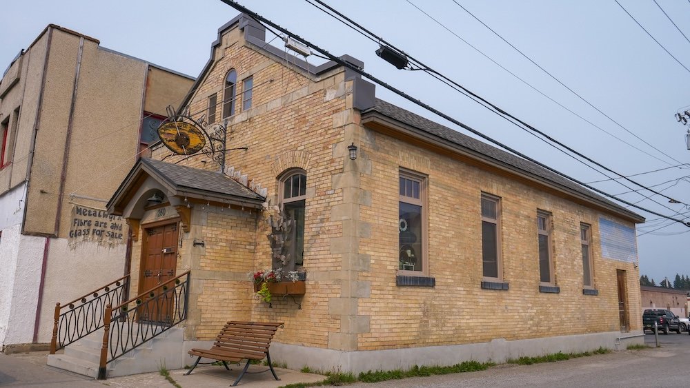 Exterior of the Eye of the Needle Studio & Gallery on 5th Street in downtown Fernie, BC, a small brick heritage-era building with arched windows and a steep gable—an easy photo stop on the self-guided walk.
