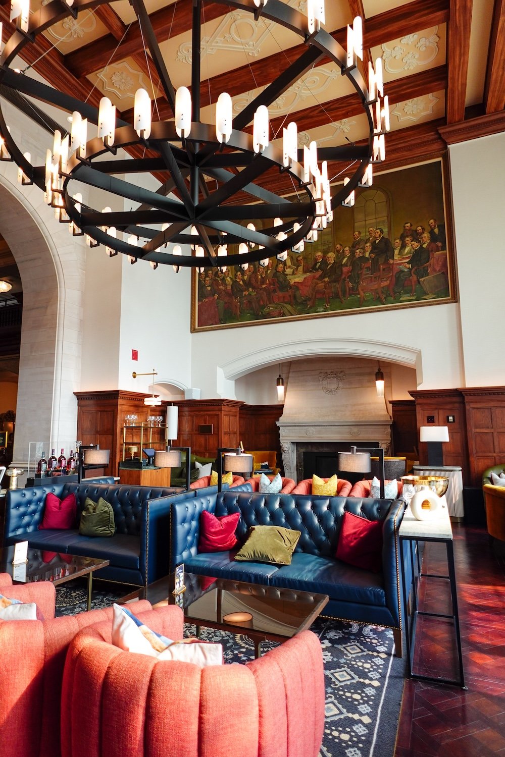 Fairmont Hotel Macdonald lounge interior Elegant interior seating at the Fairmont Hotel Macdonald features deep blue tufted sofas, vibrant accent pillows, warm wood paneling, and a dramatic circular chandelier overhead, with a historic mural adding character to this grand and inviting lounge space.